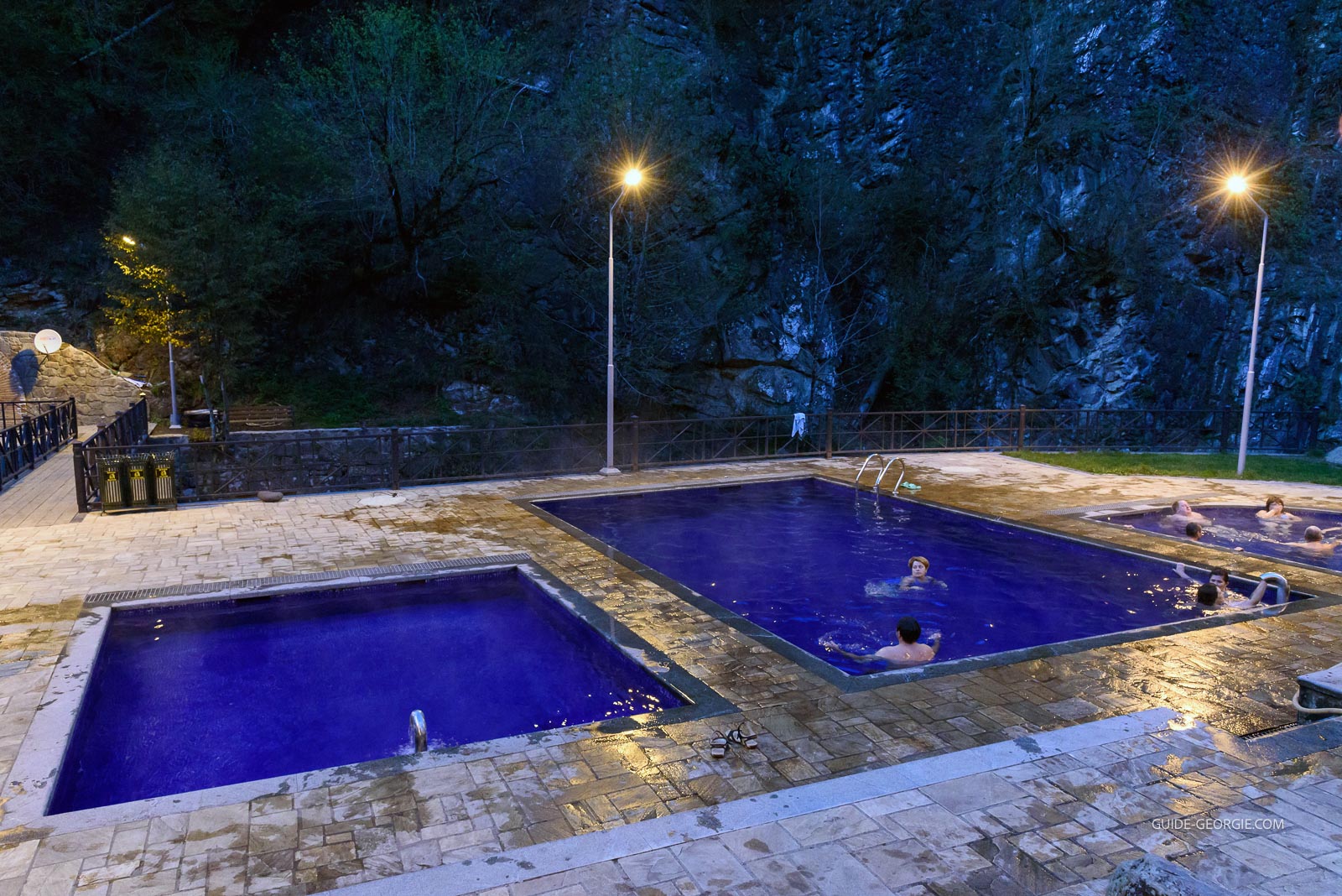 Bassins extérieurs d'eau sulfureuse dans un parc, entourés d'arbres au crépuscule