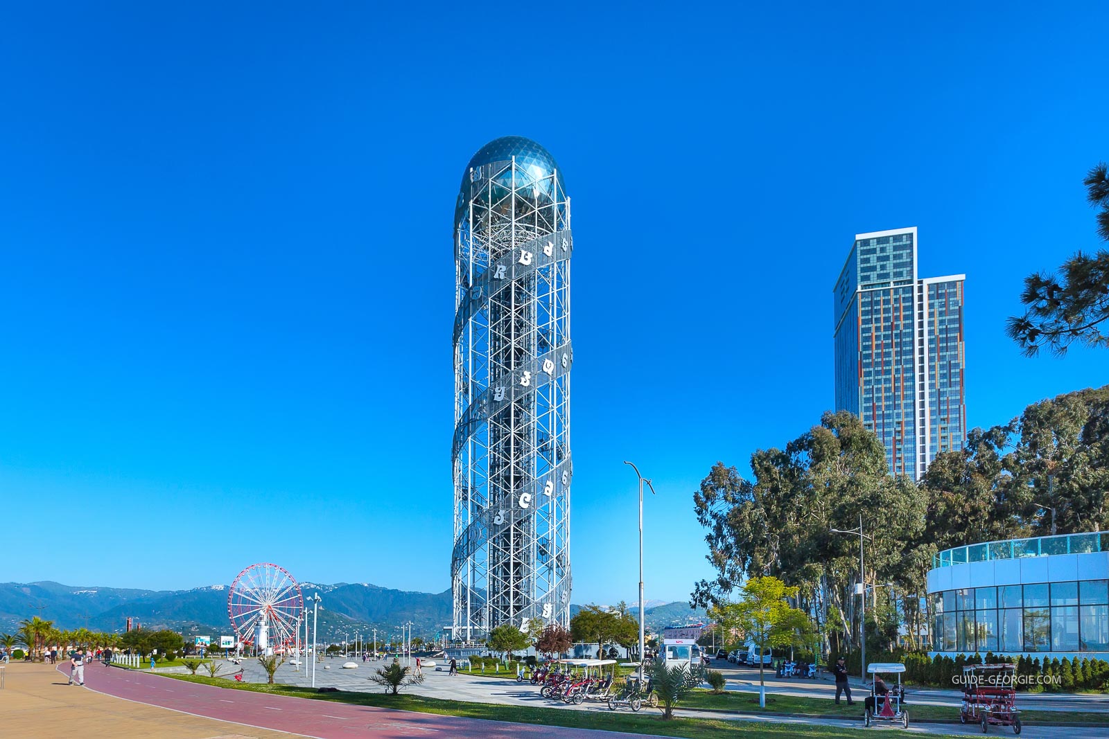 Vue en journée d'une tour moderne en forme de double hélice à côté d'une grande roue près du front de mer