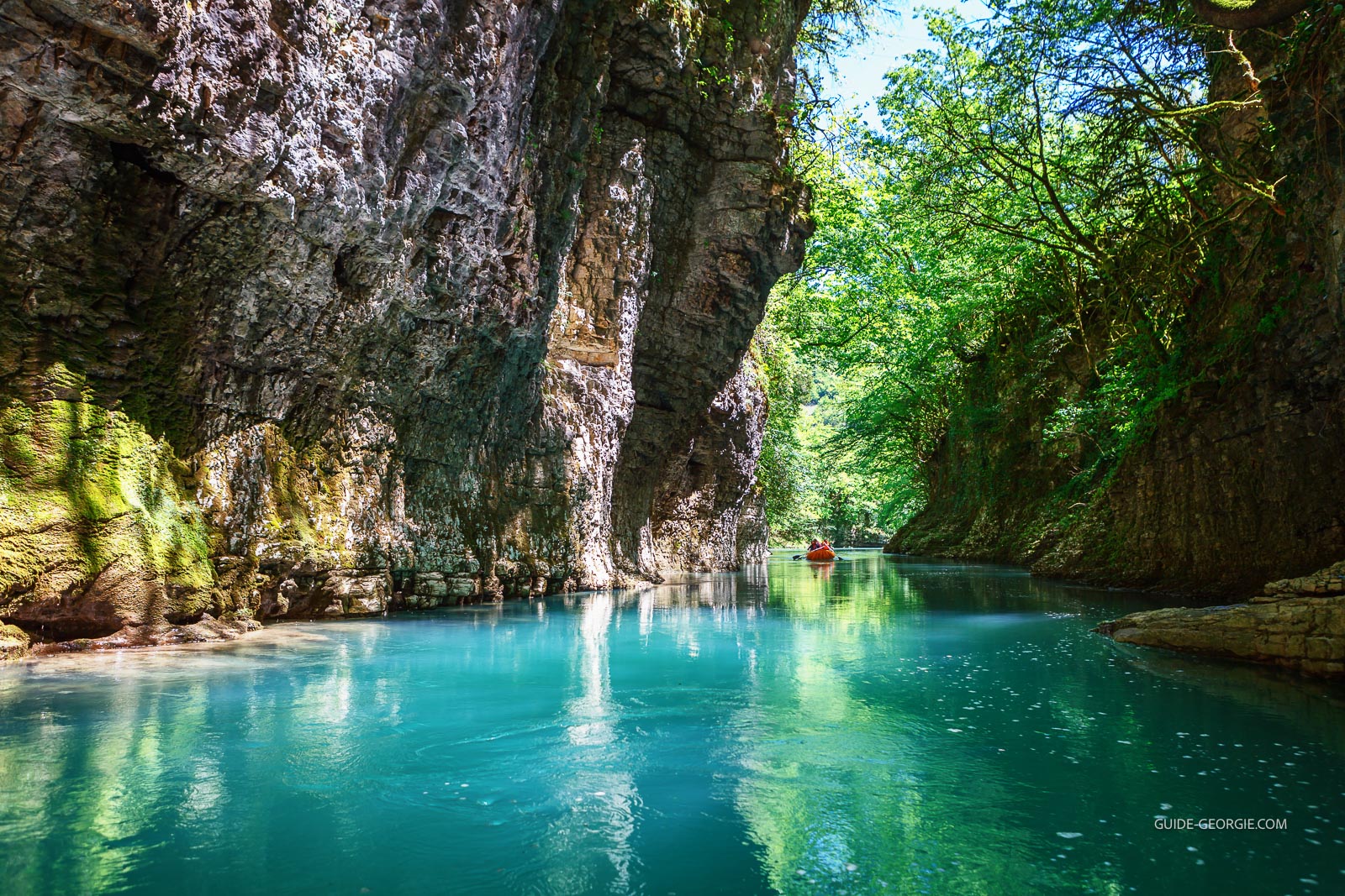 Canyon escarpé avec rivière bleu clair et petit bateau naviguant entre les parois rocheuses, berges boisées