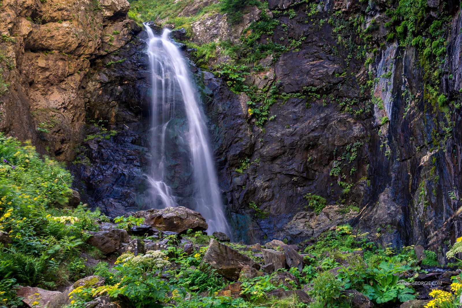 Cascade en plusieurs niveaux entourée de forêts et de montagnes dans le massif du Caucase