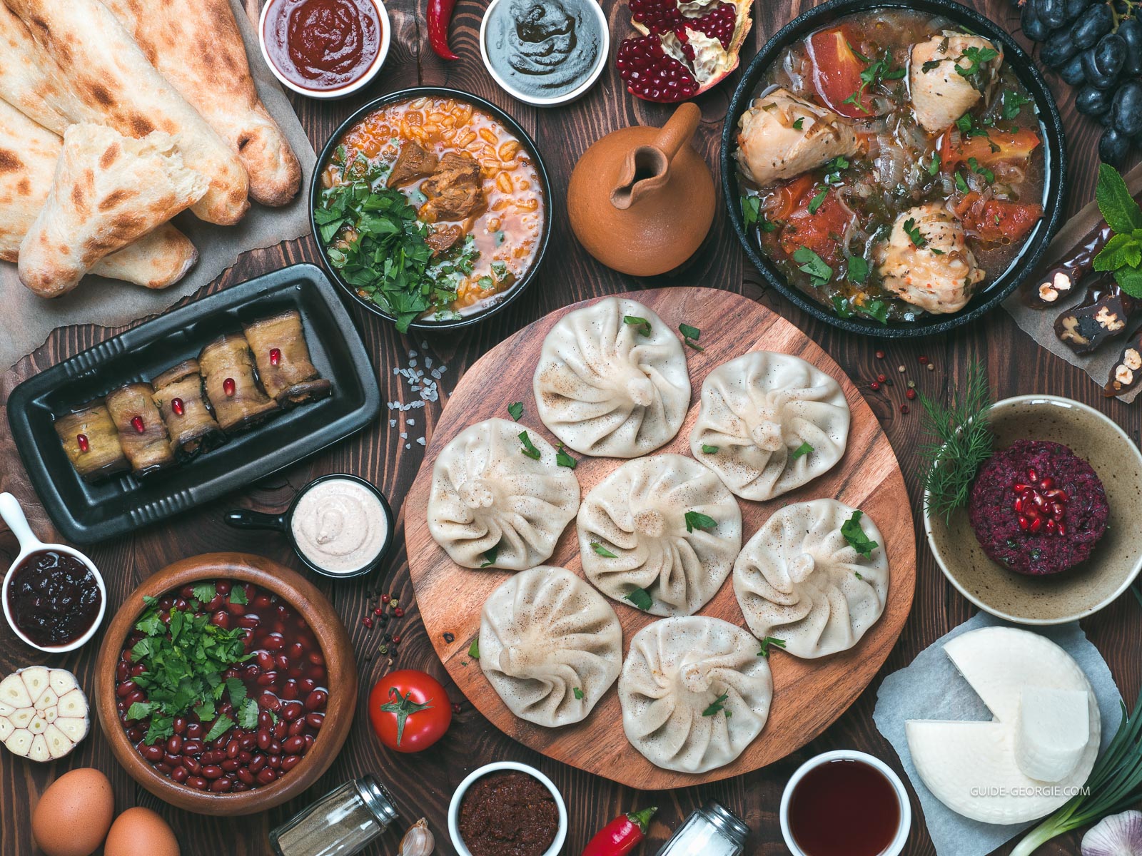 Vue plongeante de plats géorgiens sur table en bois: khinkali, plats en sauce, salades et condiments.