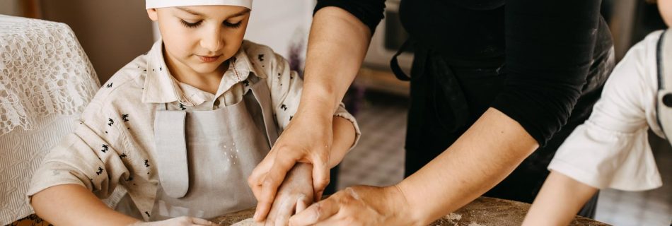 Gros plan sur un enfant façonnant une boule de pâte à pain sur une table en bois, aidé par une main adulte