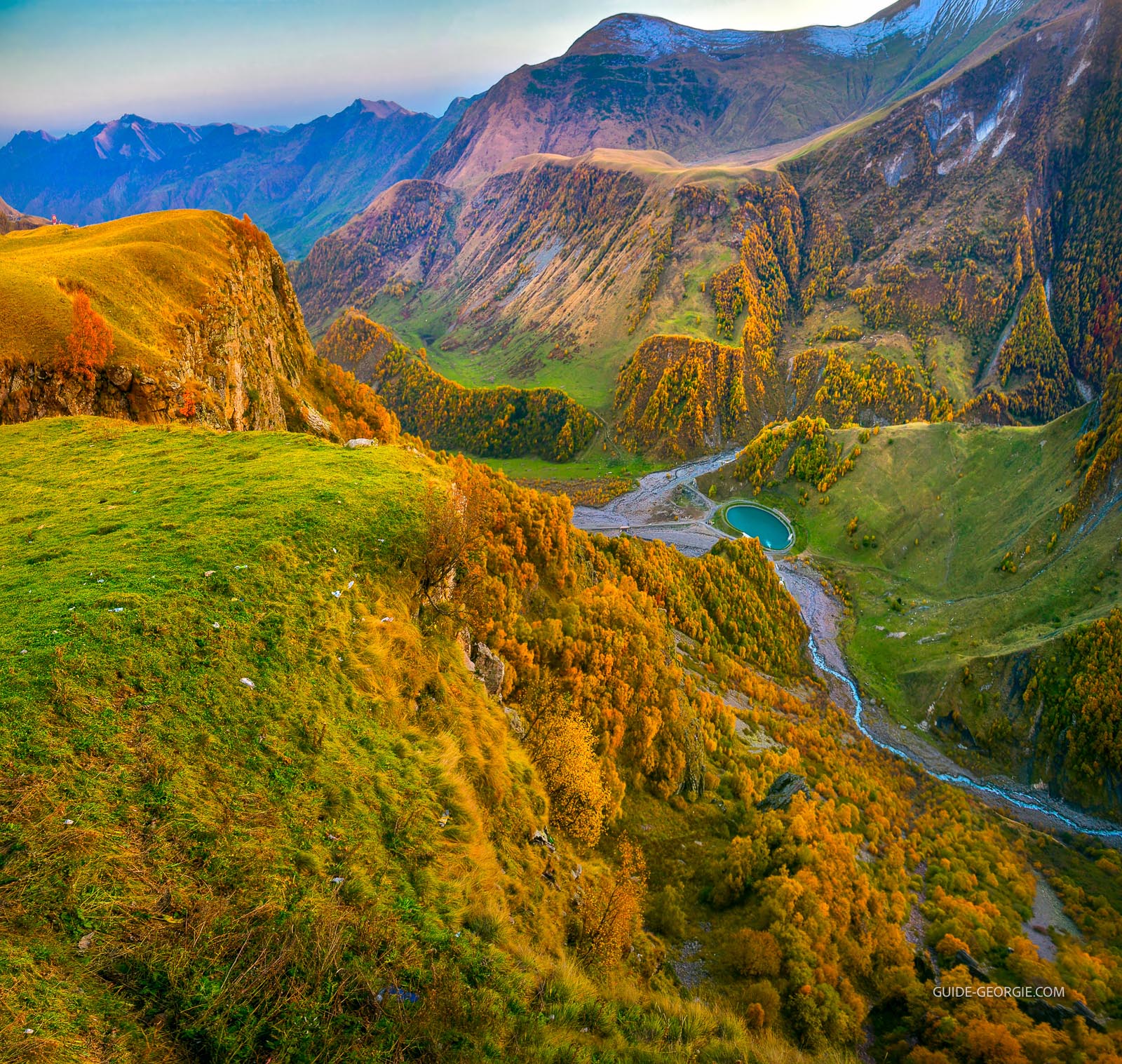 Panorama d'une gorge de montagne au coucher du soleil, forêts d'automne et petit lac au fond