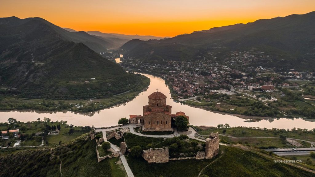 Vue aérienne du monastère de Jvari perché sur une colline, bâtiments en pierre et paysage environnant avant le coucher du soleil