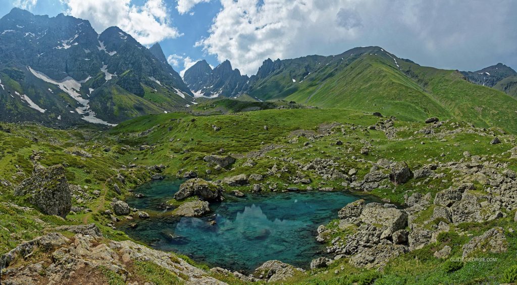 Chaîne de montagnes escarpées sous ciel nuageux avec pâturages et lacs en contrebas