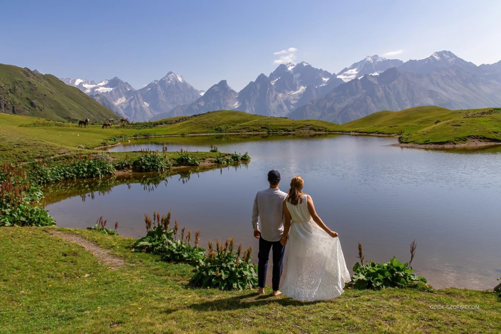 Couple de mariés au bord d'un lac de montagne, chevaux au rivage et vallées montagneuses en arrière-plan