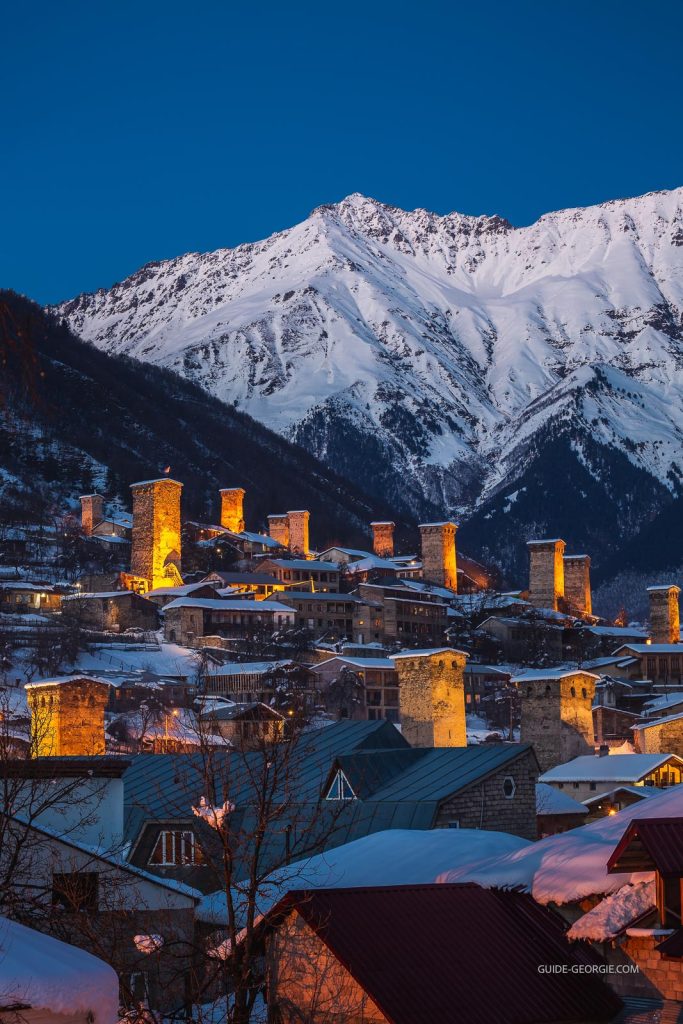 Vue aérienne de Mestia au crépuscule, maisons et reliefs montagneux sous une lumière bleutée