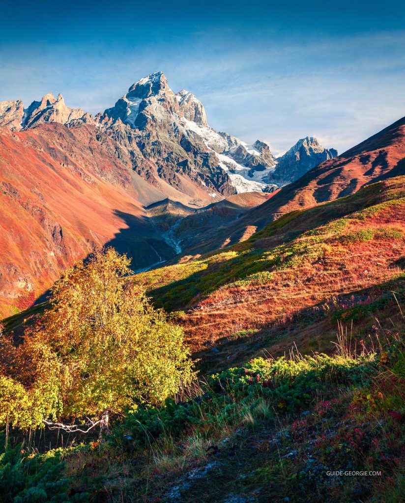 Pic montagneux pointu dominant le paysage sous un ciel bleu profond et lumineux, matin d'automne dans les montagnes du Caucase.