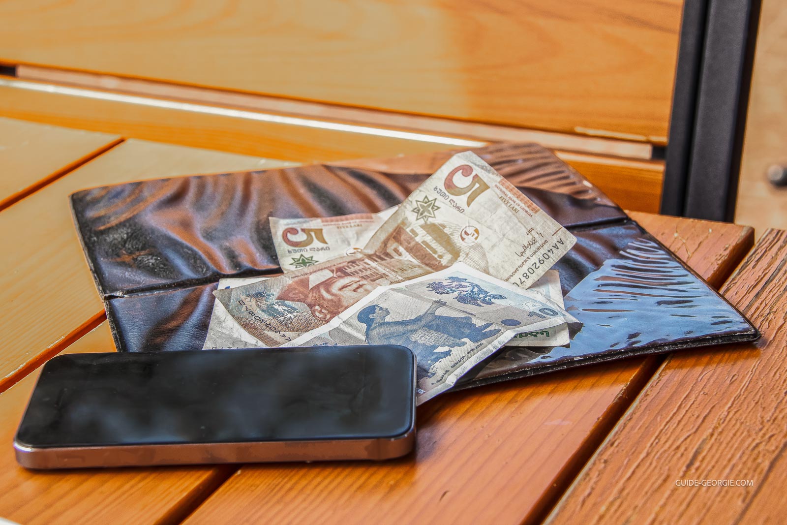 Billets en lari géorgien posés sur une table en bois à côté d'une pochette plastique contenant l'addition et d'un téléphone portable.