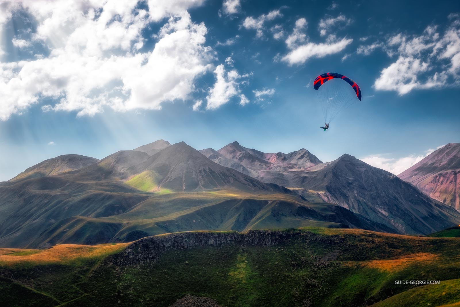 Un parapente en vol au-dessus de montagnes escarpées sous un ciel lumineux avec des rayons de soleil