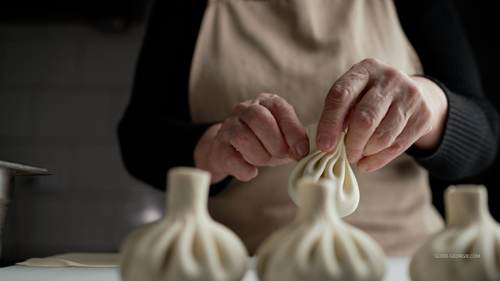 Gros plan sur des mains féminines façonnant des khinkali, boulettes de pâte crue posées sur un plan de travail