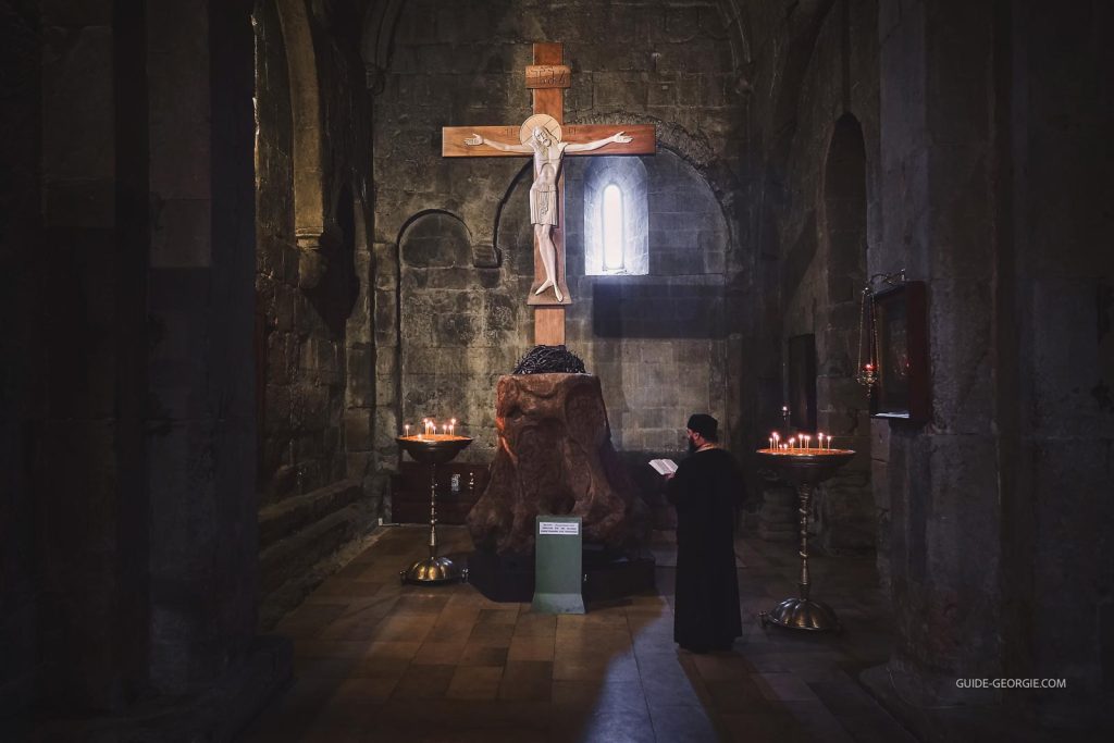 Prêtre en soutane agenouillé près d'une croix en pierre à l'intérieur d'une cathédrale