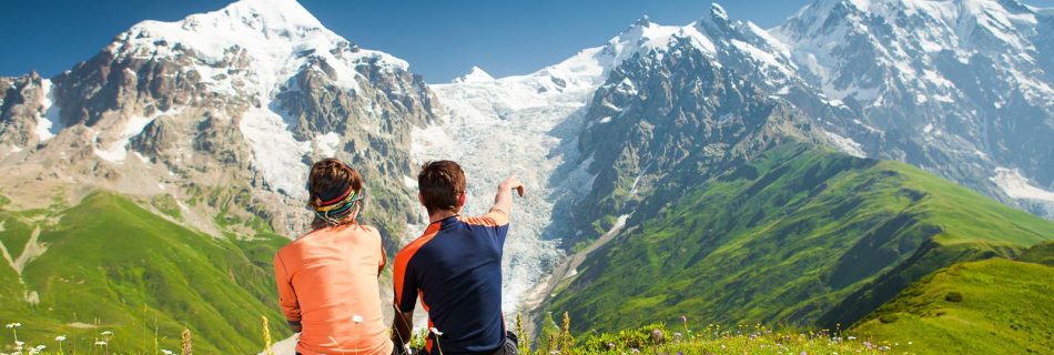 Un couple en tenue de randonnée assis sur un rocher, contemplant un paysage montagneux sous des nuages