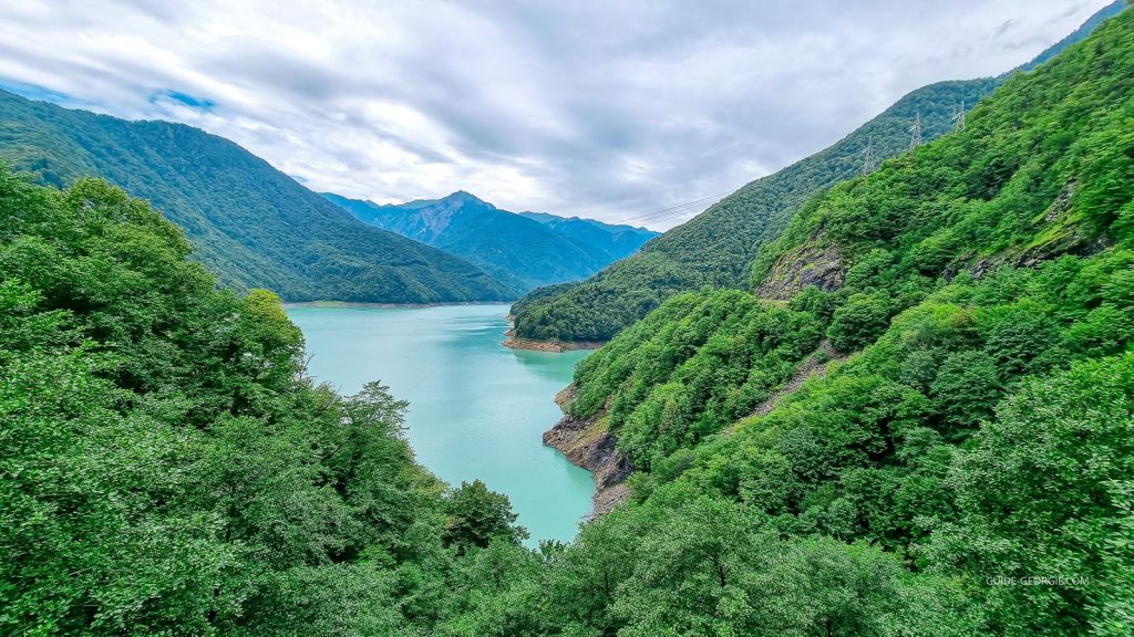 Lac turquoise entouré de montagnes du Caucase central avec une route longeant la rive