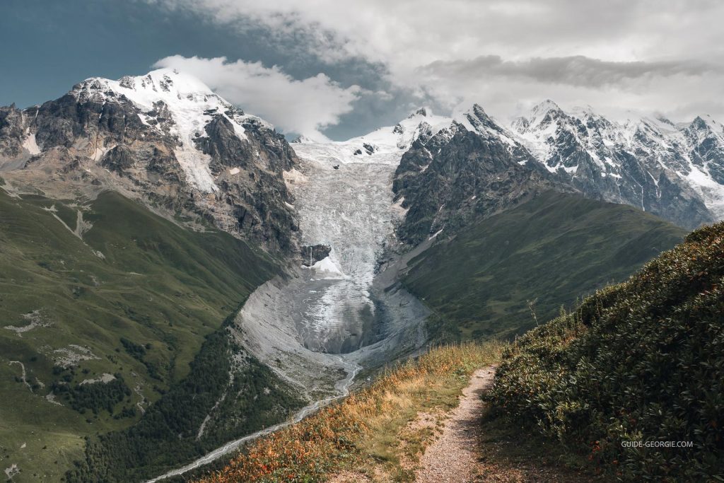 Vue du glacier Shkhara entouré de sommets enneigés et de zones de fonte de glace sous un ciel couvert