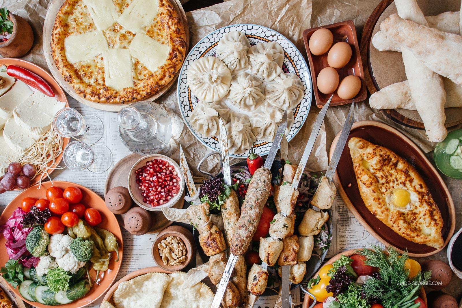 Vue du dessus d'une table en bois couverte de nombreux plats et ingrédients de cuisine géorgienne, légumes, fromages et pains