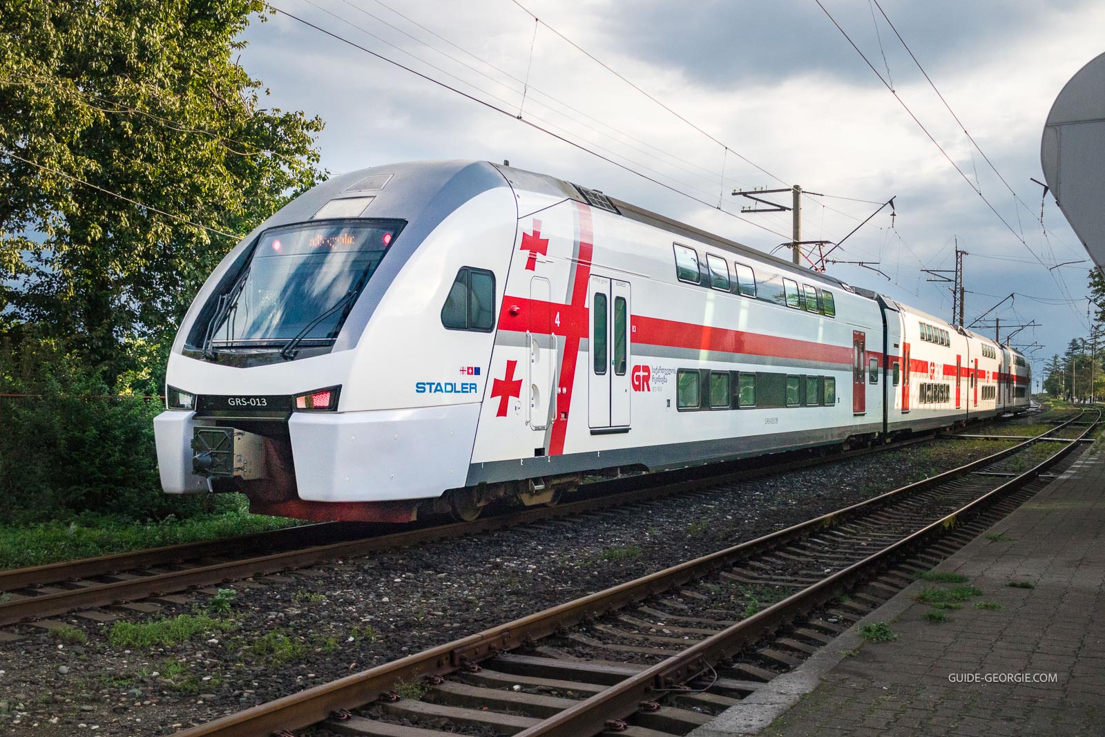 Train moderne de la compagnie ferroviaire géorgienne circulant en bord de ville avec passagers à bord